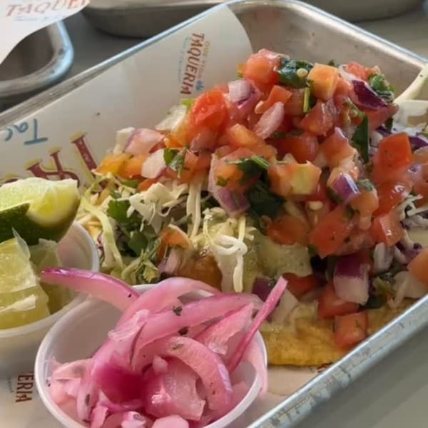 Que Vida Taqueria fish taco with pico de gallo, shredded cabbage, lime wedges, and pickled onions.
