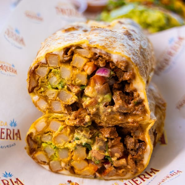 A Que Vida Taqueria burrito, cut in half, revealing steak, potatoes, avocado, and red onion.