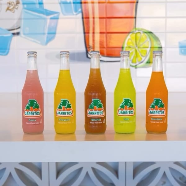 Five colorful Jarritos soda bottles, including guava, pineapple, tamarind, lime, and mandarin flavors.